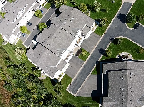 Aerial view of a residential neighborhood showing the top view of houses with grey roofs, driveways, and well-kept green lawns, with roads intersecting the orderly layout